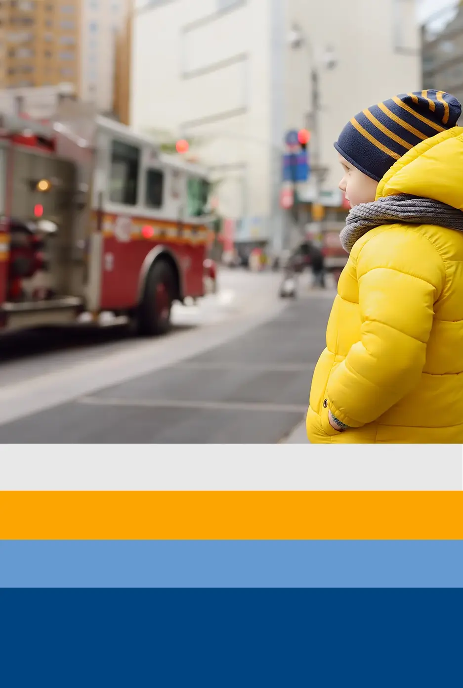 Child wearing a yellow jacket stands on the street, gazing in admiration as a fire truck passes by. This scene illustrates how BTC collaborates with families of first responders, aiming to enhance the mental well-being of all involved