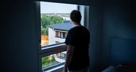 Man appearing depressed in the dark looking outside from a window