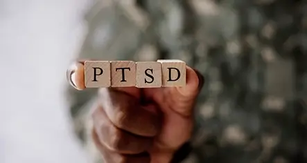 Military person's hand holding 4 cubes spelling out PTSD to show that BTC offers treatment for PTSD