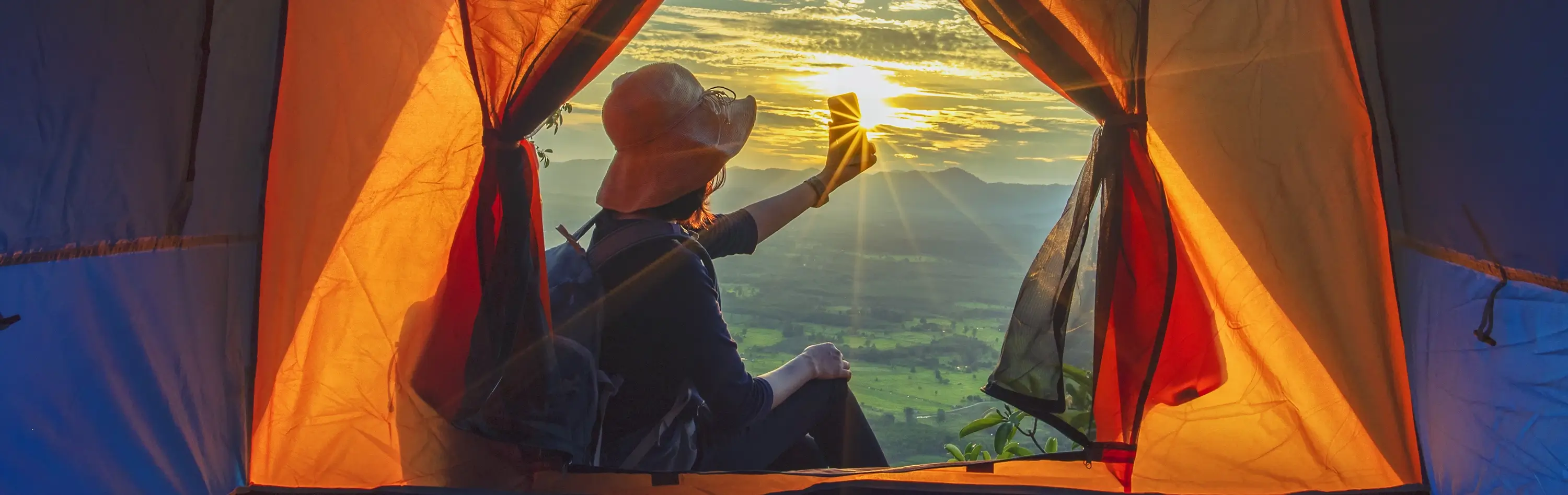 A woman capturing a sunrise outside her tent in nature epitomizes the fulfillment attainable when prioritizing mental wellbeing.