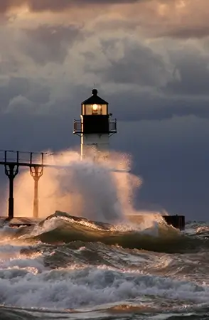 A wave crashing onto a lighthouse amidst stormy seas, representing the internal turmoil experienced by individuals with PTSD, yet emphasizing the hope offered by our mental health clinic